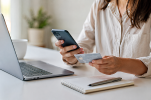 Illustration réaliste et minimaliste représentant une jeune femme française utilisant une application bancaire sur son smartphone dans un intérieur moderne et lumineux. L’ambiance est élégante et apaisante, avec des tons neutres et une lumière naturelle douce. Une carte bancaire discrètement visible à côté du téléphone évoque les Cartes de crédit et les services financiers numériques simplifiés. L’image transmet une sensation de confiance, de fluidité et d’accessibilité liée au financement personnel en France.